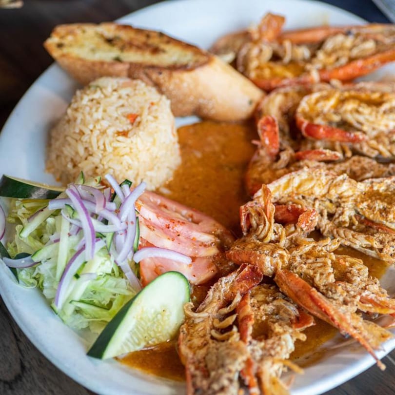 A plate of Mexican food with grilled lobster, rice, garlic bread, and a side salad.