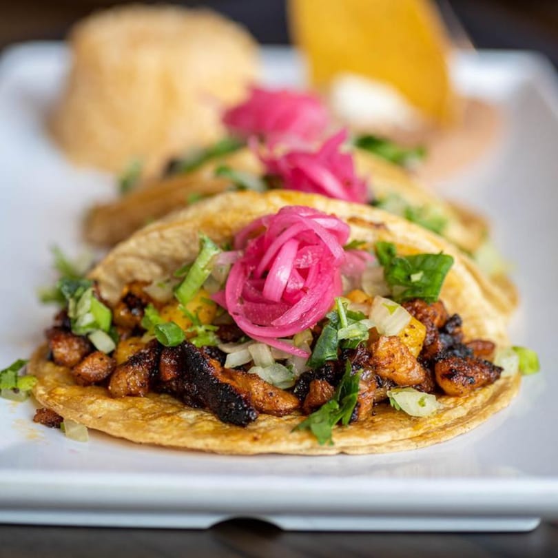 Three Alejandra's Mexican Restaurant tacos with grilled meat, onions, cilantro, and pickled red onions.