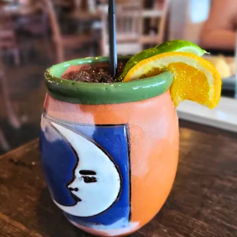 Mexican cantarito cocktail in a colorful ceramic mug with a moon design, garnished with citrus.