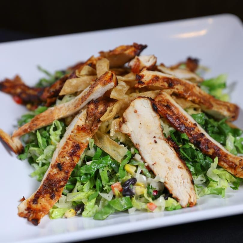 Grilled chicken strips and crispy tortilla pieces on a bed of fresh lettuce, corn, and black beans.