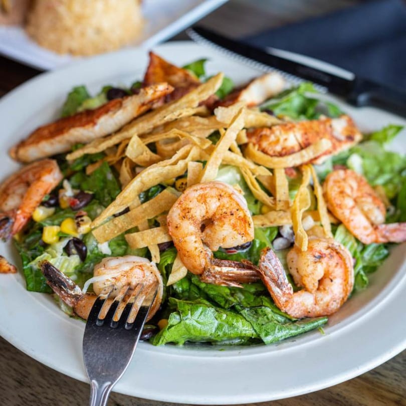 A vibrant Mexican shrimp salad with lettuce, corn, black beans, and tortilla strips.