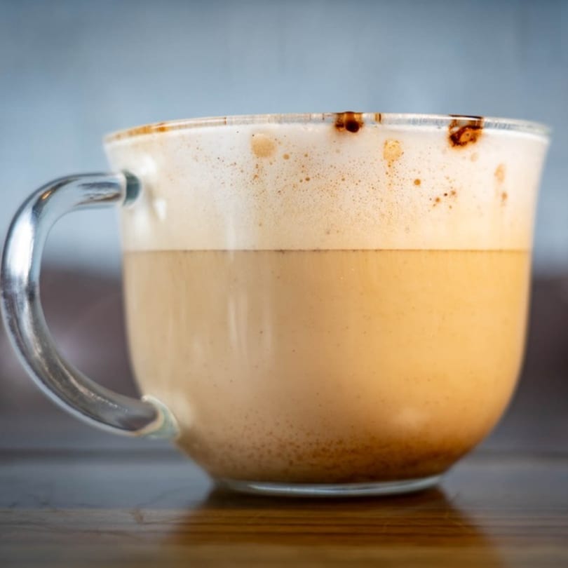 A clear mug of Mexican coffee with a thick layer of foam and chocolate drizzles.